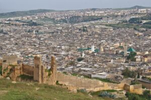 Panoramic view over the dense rooftops, minarets and green-tiled roofs of Fès el-Bali, seen from the ruined walls near the Merinid Tombs