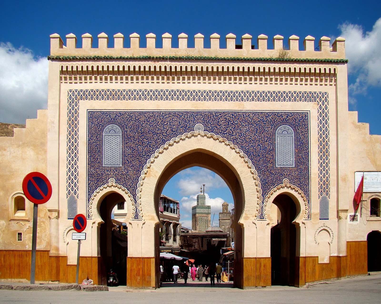 The triple horseshoe arches of Bab Bou Jeloud in Fez, covered in blue zellij tilework, with minarets visible through the central arch