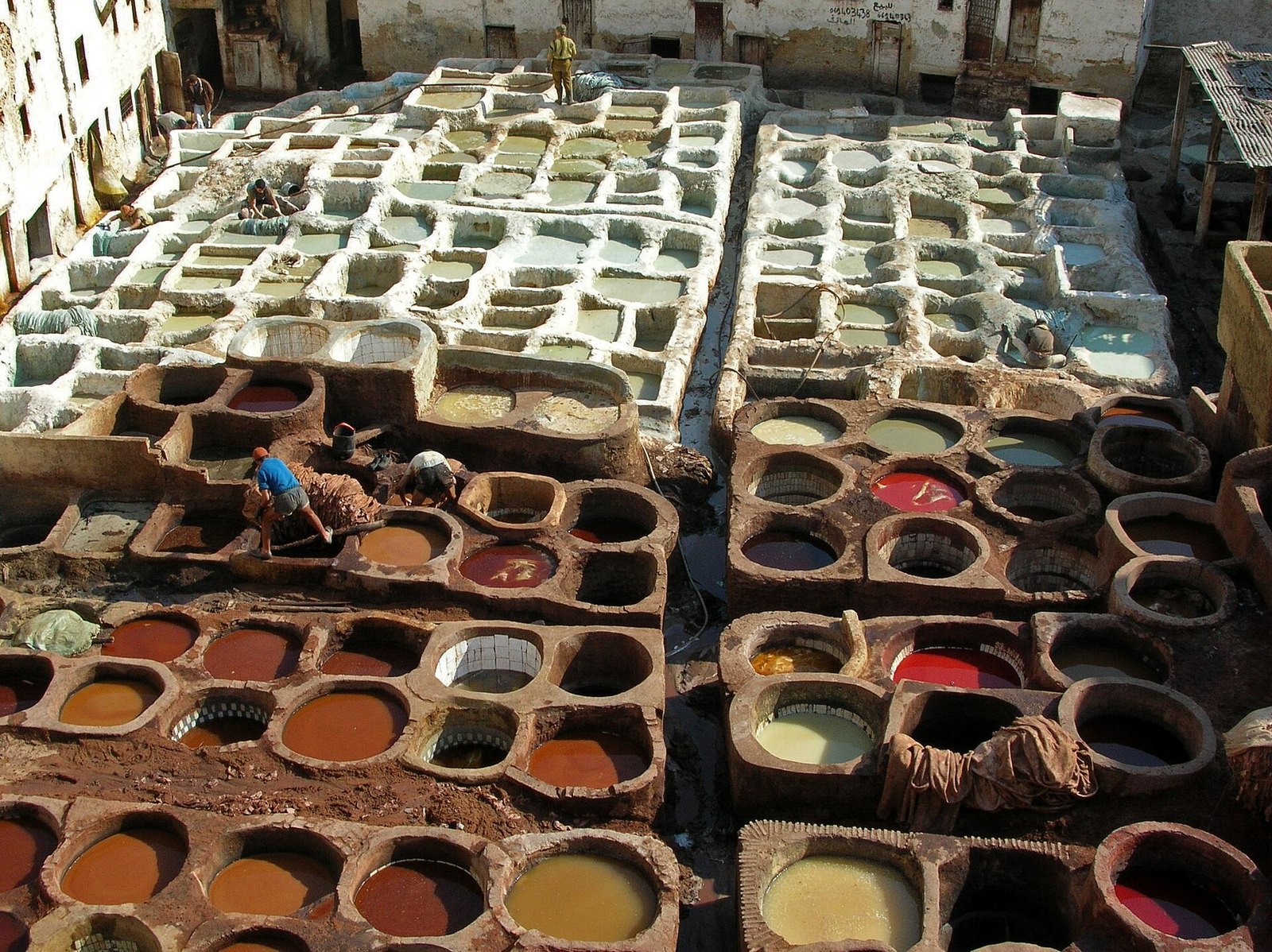 Rows of round stone vats filled with white, red, yellow and brown dyes at a traditional leather tannery in FÃ¨s el-Bali, with workers among them