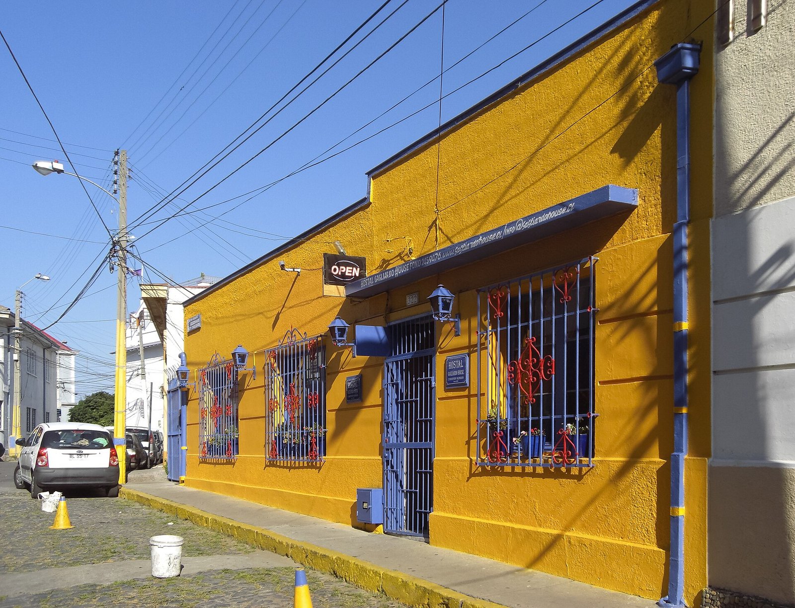 Yellow house with blue trim and barred windows on a sloping cobbled street in Cerro Alegre, Valparaíso